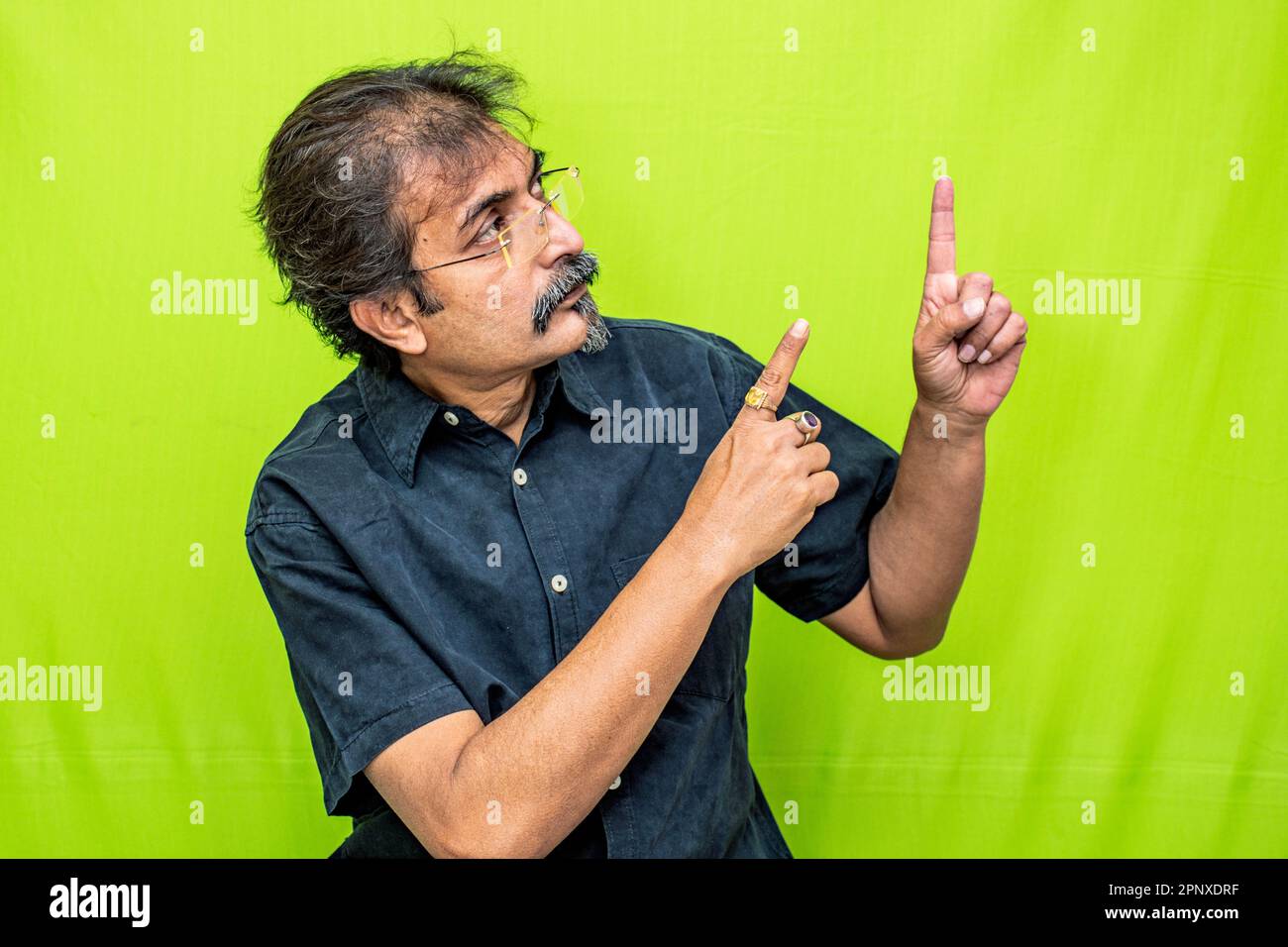 Smart businessman in the black shirt on the green screen points with both hands toward the top-left direction Stock Photo