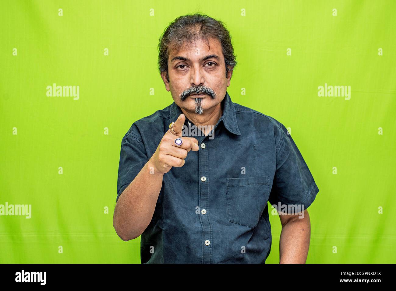 Confidently standing against a green screen, a smart corporate businessman in a black shirt points forward with his right hand, exuding professionalism Stock Photo