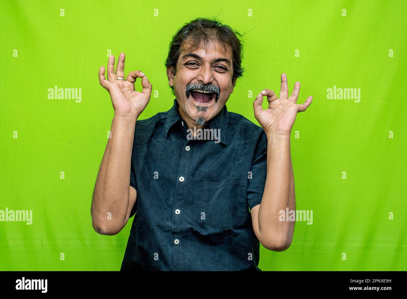 The corporate man in black shirt looks joyful and charming, laughing and gesturing with hands against a green screen background Stock Photo