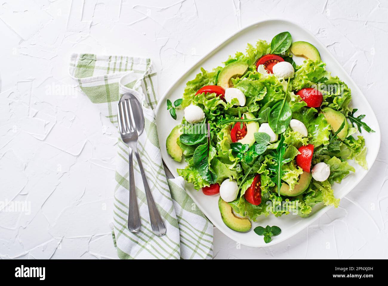 Fresh green salad with avocado, mozzarella cheese and tomato on white table background Stock Photo