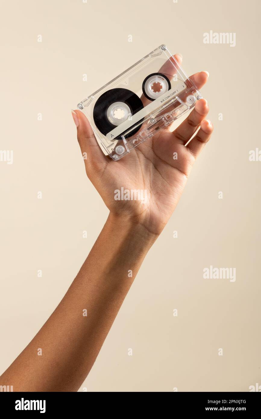 Unrecognizable African American female with vintage cassette tape in hand against beige background Stock Photo