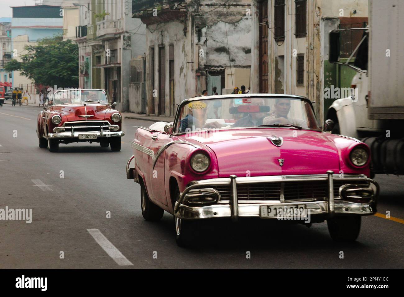 The classic cars driving down a street, lined with old-fashioned buildings Stock Photo