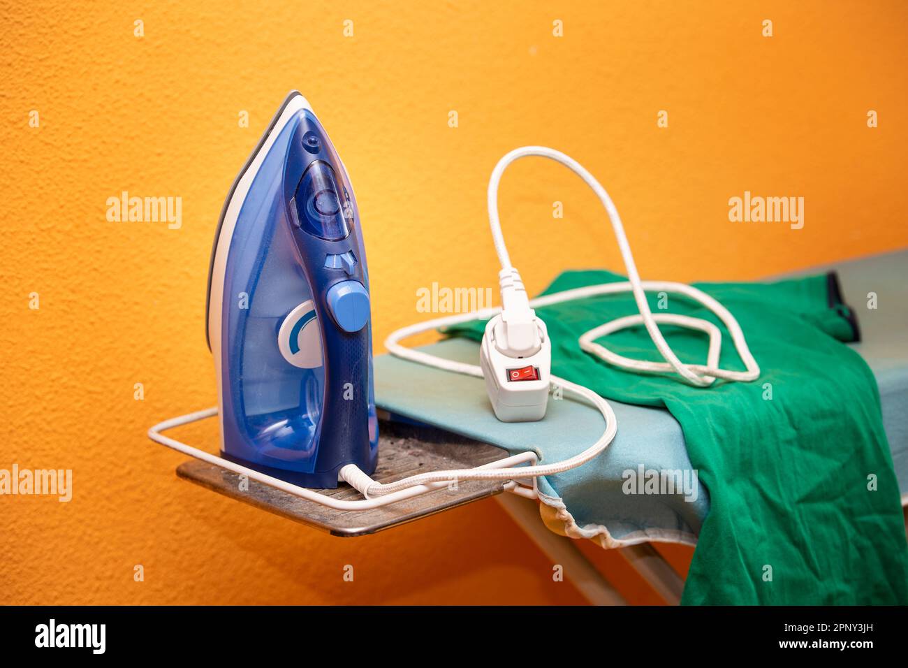 blue steam iron on ironing board unplugged and with wrinkled clothes Stock Photo