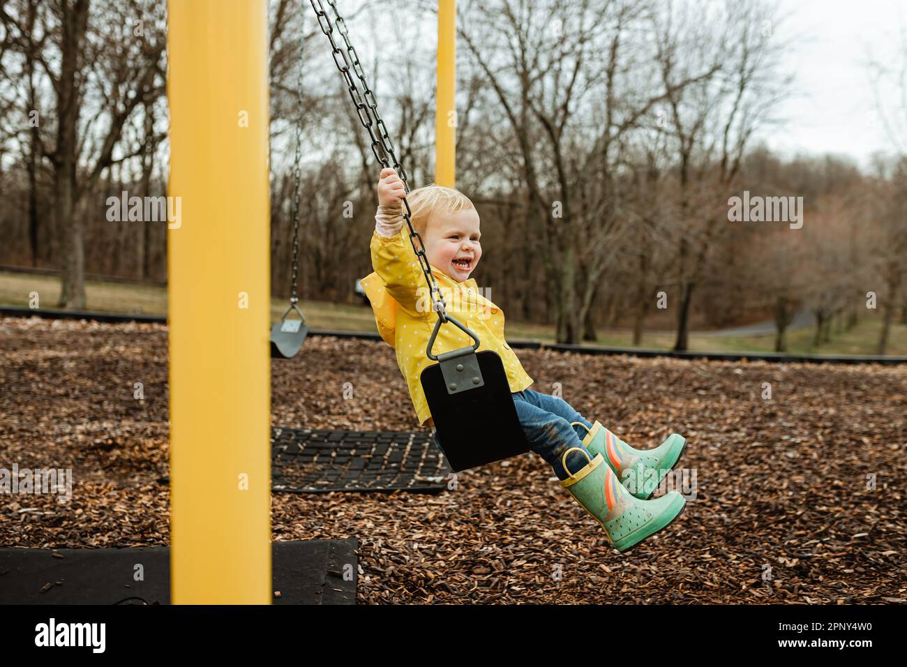 Happy child swinging in rain jacket and boots during spring Stock Photo