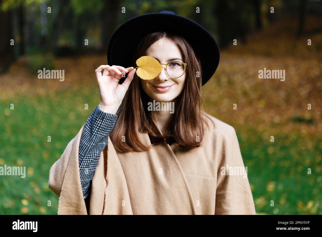 brown-haired woman in a black hat and poncho walks in  autumn park Stock Photo