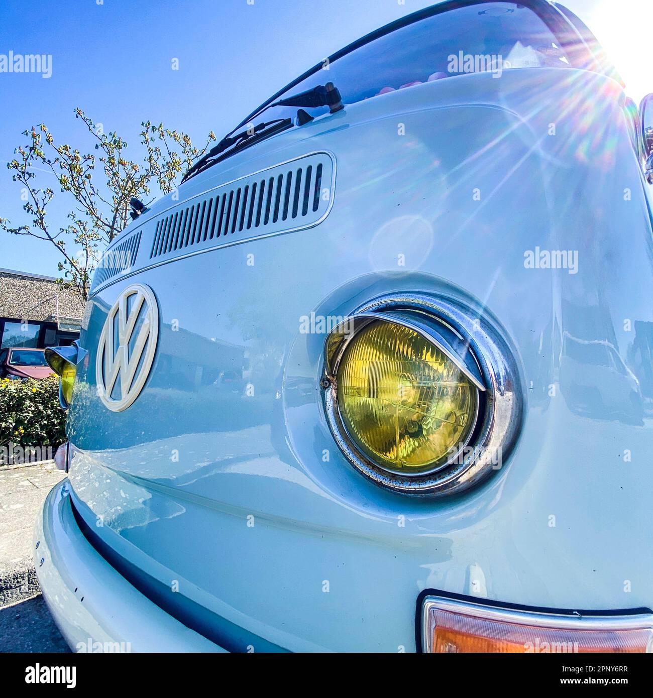VW Bus Type2 T2a Bulli in himmelblau mit gelbem Hauptscheinwerfer und weißem VW-Zeichen im Sonnenlicht. Der Kult-Bulli ist das frühe Modell vor 1971, . Stock Photo