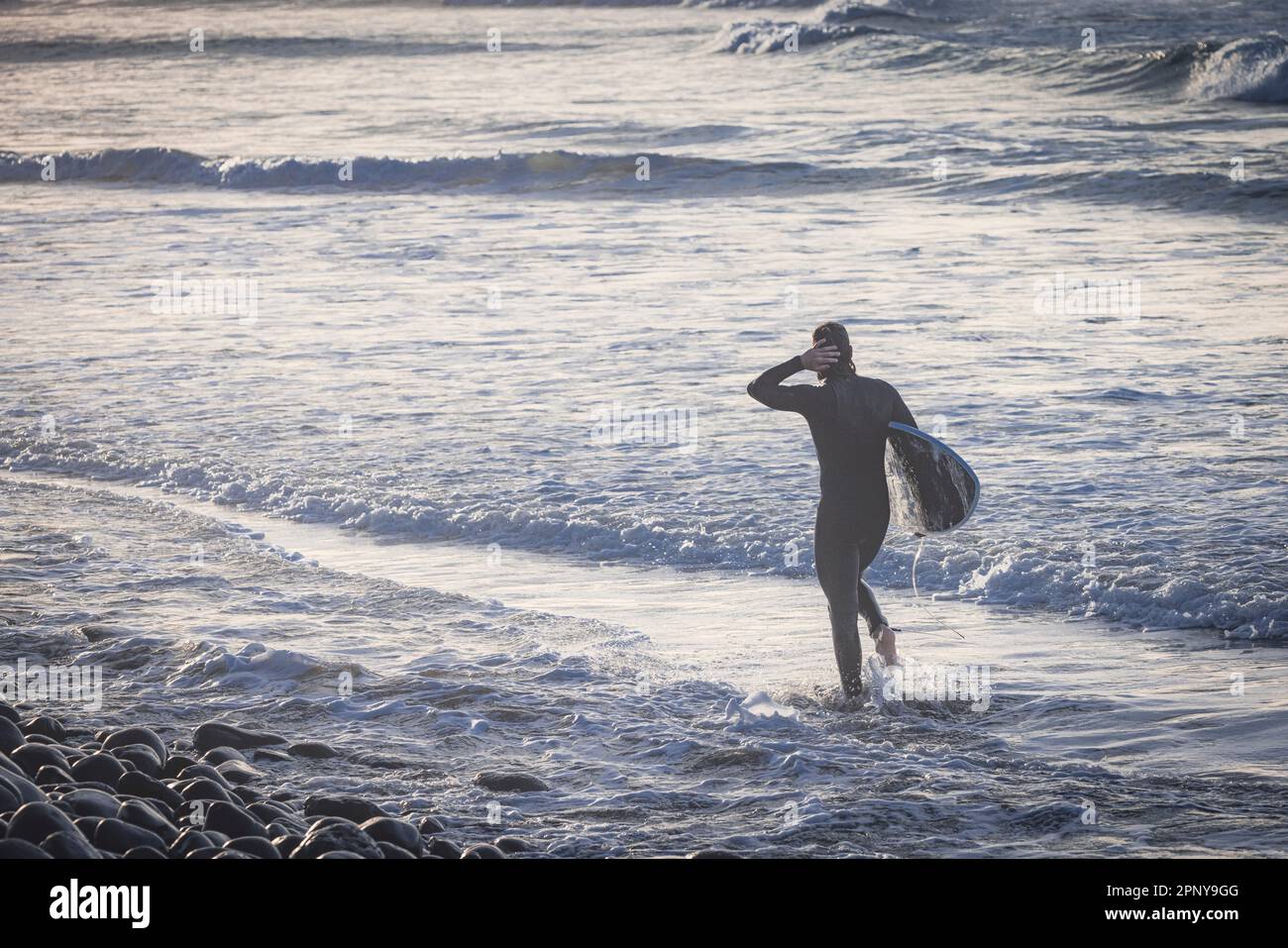 surfer coming out of the water at sunset Stock Photo