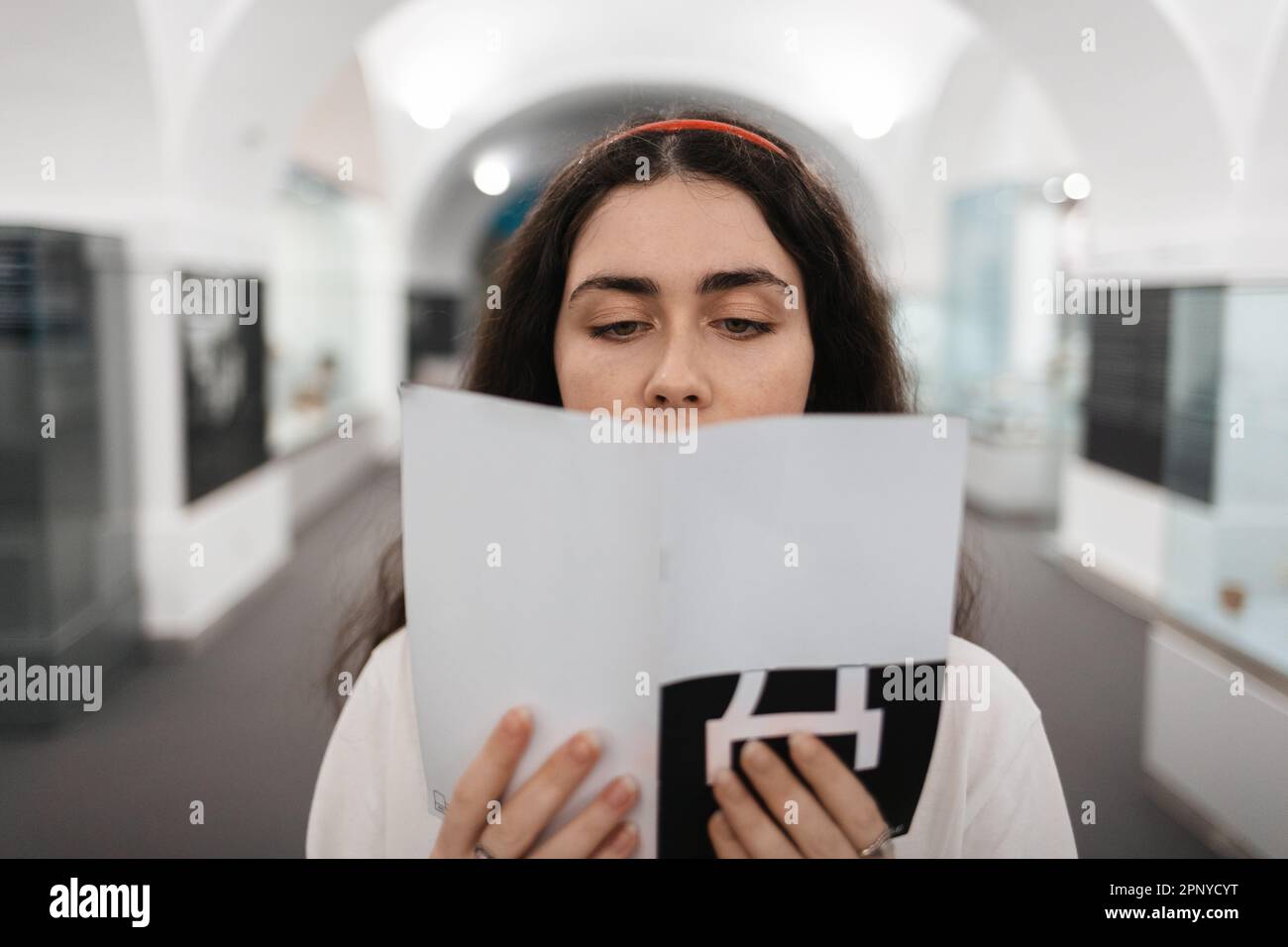 Portrait of young Caucasian woman holding brochure in her hands and reading it. Concept of cultural education and museum's day. Stock Photo