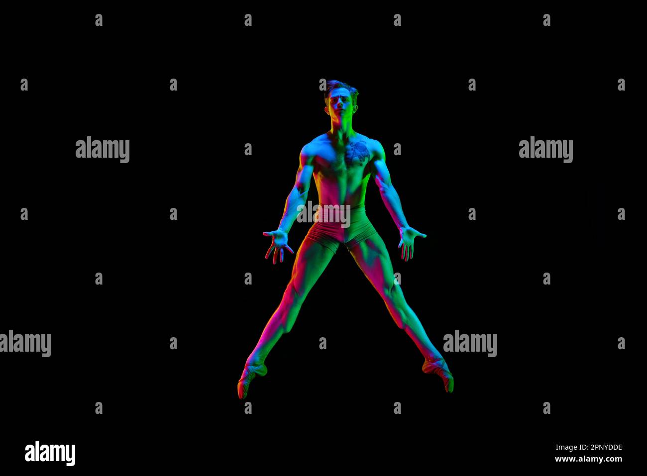 One attractive young male, ballet dancer jumping star pose in air over dark studio background with neon light. Multicolored body Stock Photo