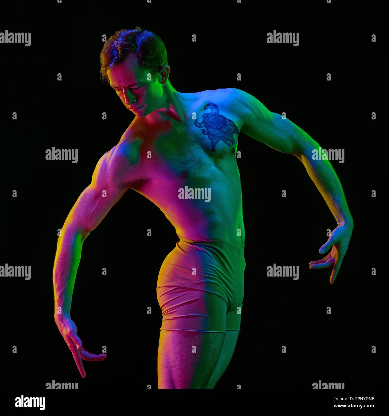 Portrait of graceful muscled male ballet dancer dancing over dark studio background with neon light. Back view. Weightless, flexible actor Stock Photo