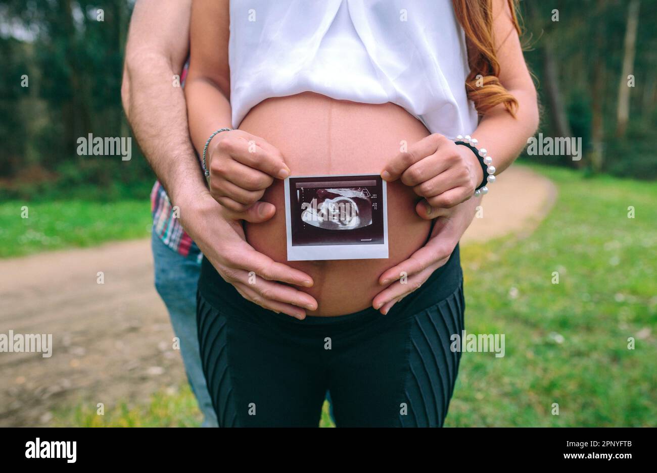 Female pregnant showing ultrasound scan of baby while her partner holding her belly Stock Photo