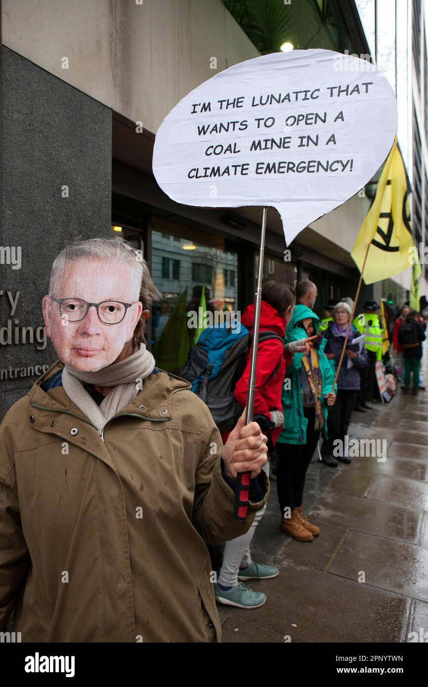 London, UK. 21st Apr, 2023. Extinction Rebellion protesters defied the rain in Westminster, with groups of protestors targeting different government ministries. A protestor wearing a Michael Gove mask holds a sign saying 'I'm the lunatic that wants to open a coal mind in a climate emergency.' Protests will continue for the next 4 days. Credit: Anna Watson/Alamy Live News Stock Photo