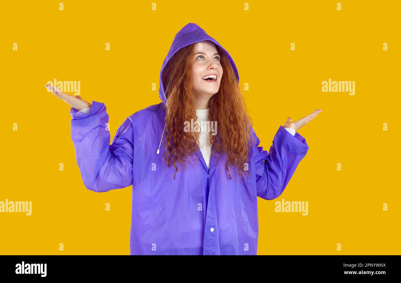 Happy young woman in purple raincoat looking up, spreading her hands ...