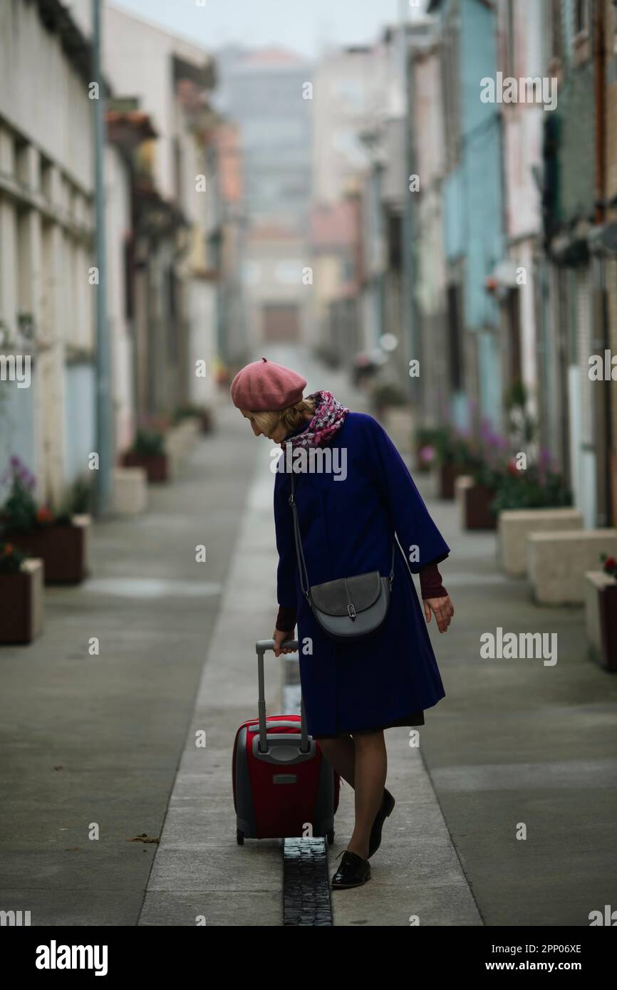 A woman rolls a suitcase down the street. Stock Photo