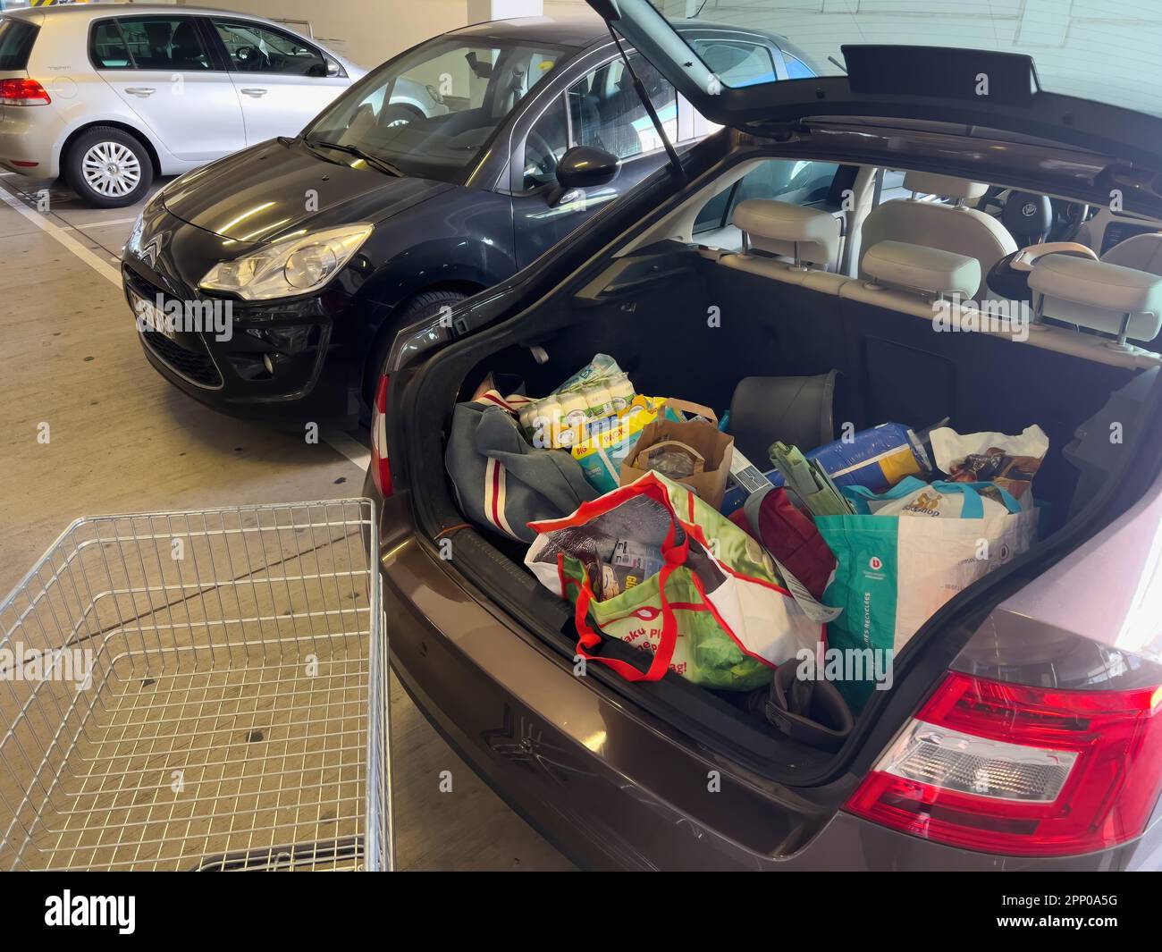 A car is parked with its trunk open, overflowing with groceries a