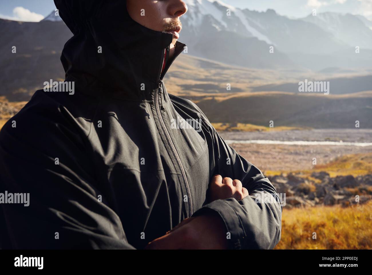 Anonymous Portrait of young man hiker tourist in black jacket standing against beautiful sunset in the mountain valley. Outdoor and trekking concept. Stock Photo