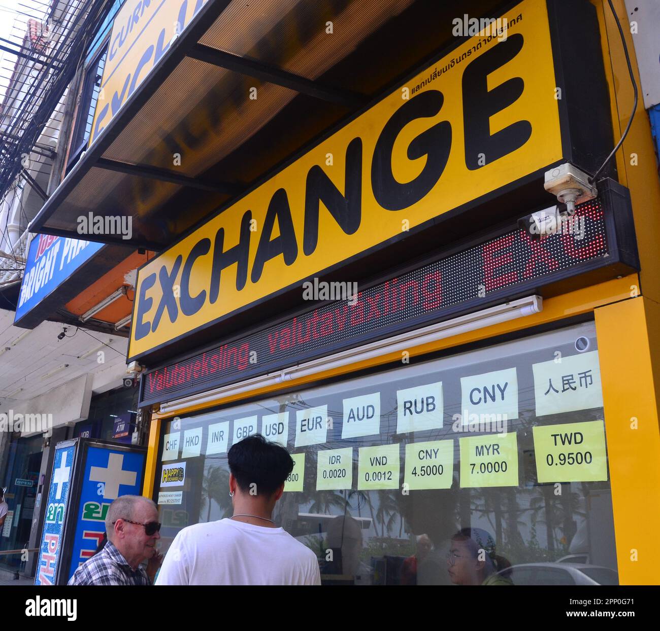 People look into a foreign exchange booth or shop where people can change currencies in Jomtien, Pattaya, Thailand, Asia. Most people are bringing their currency to exchange for Thai baht. Stock Photo