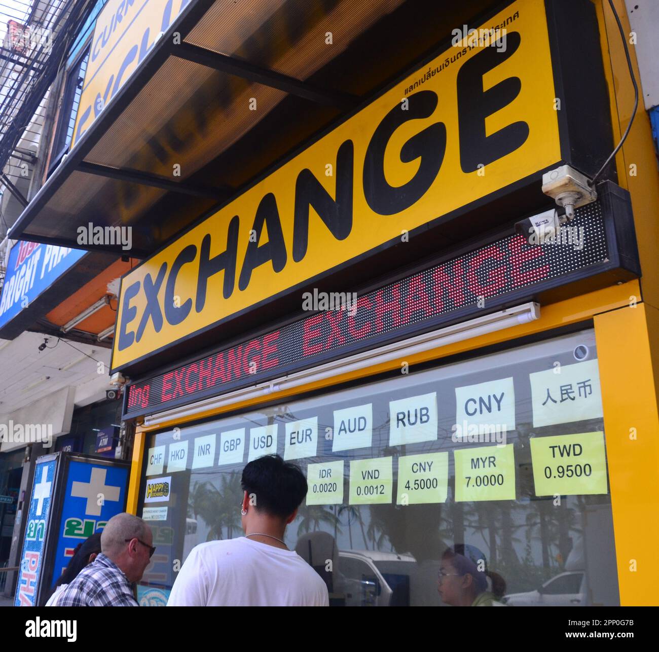 People look into a foreign exchange booth or shop where people can change currencies in Jomtien, Pattaya, Thailand, Asia. Most people are bringing their currency to exchange for Thai baht. Stock Photo