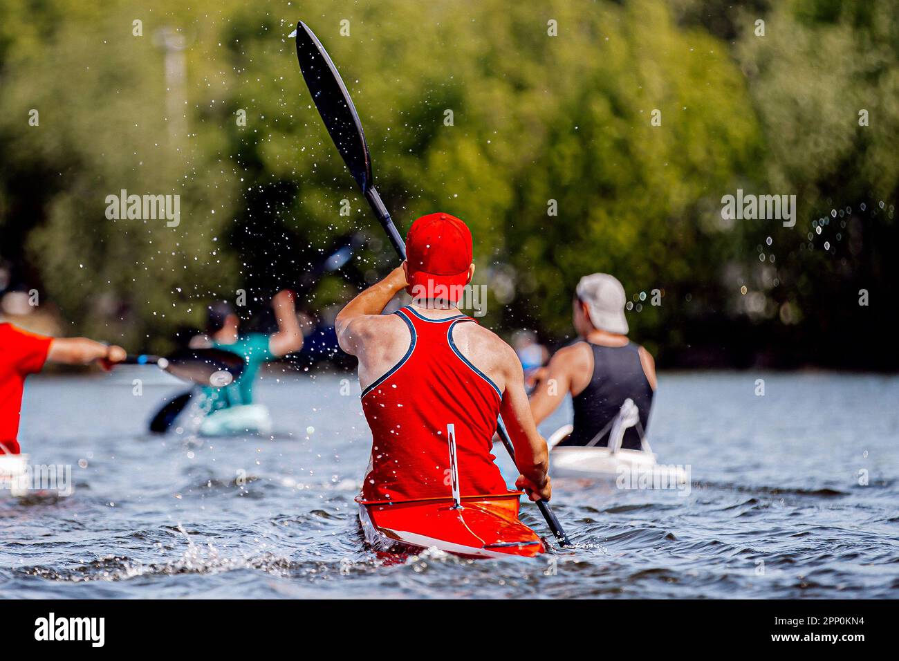 rear view group athletes kayakers on kayak single rowing training on lake, splashes and drops water from paddles Stock Photo