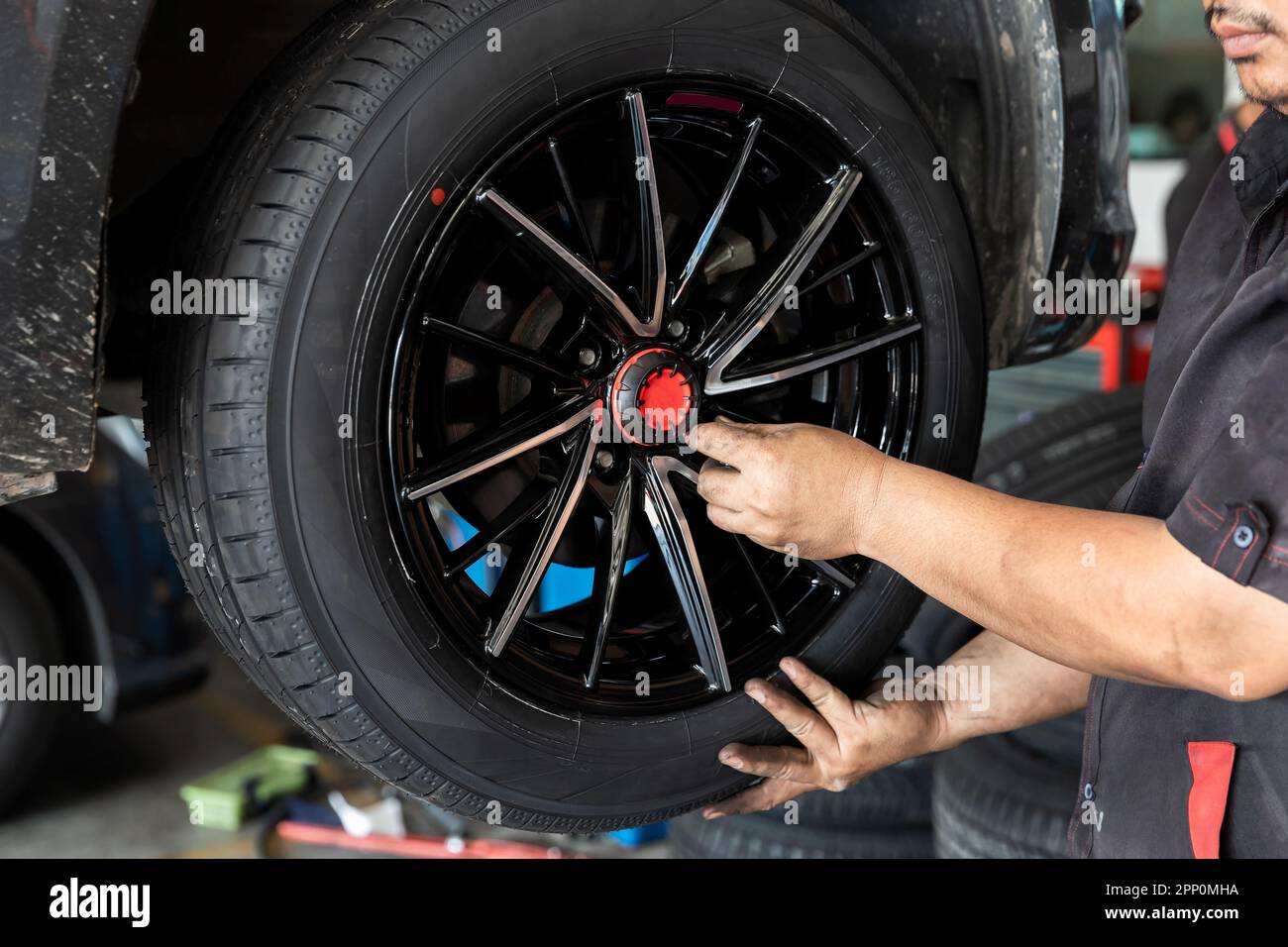 Car service, repair and maintenance concept - auto mechanic man changing tire in auto repair shop. Stock Photo