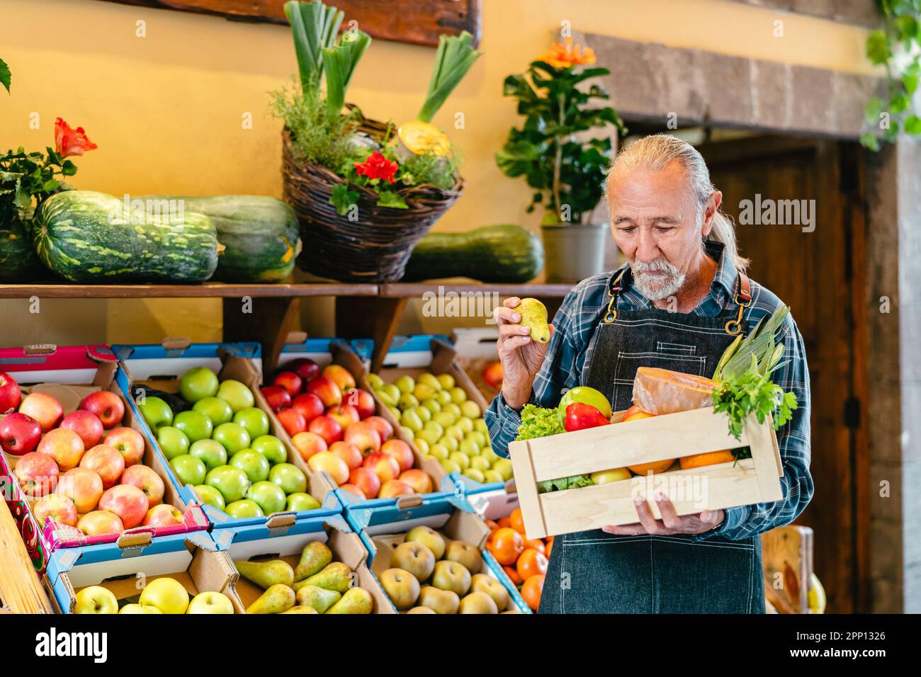 Senior greengrocer working at the market holding a box containing fresh ...
