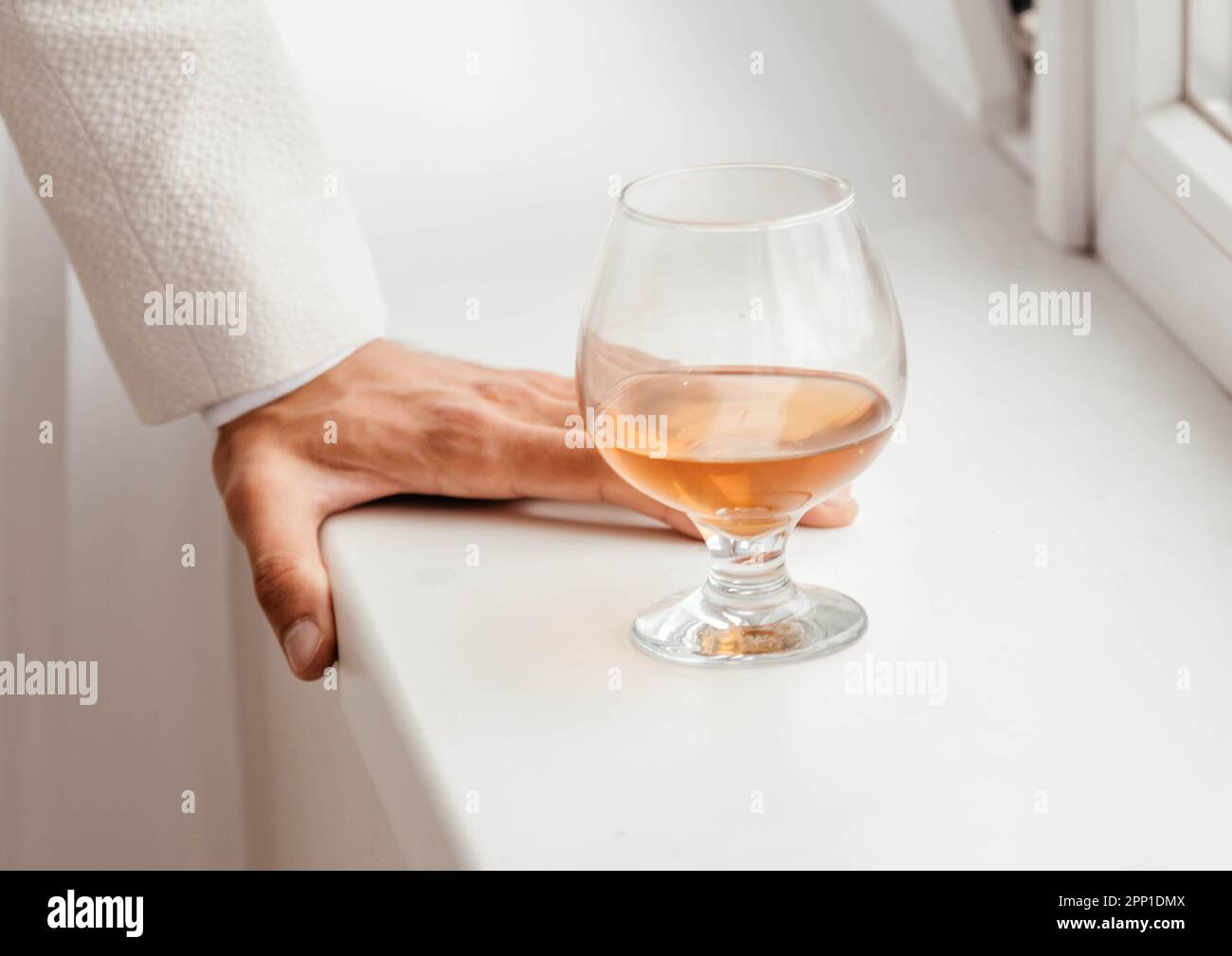 A glass of cognac on the windowsill next to a man's hand.  Stock Photo