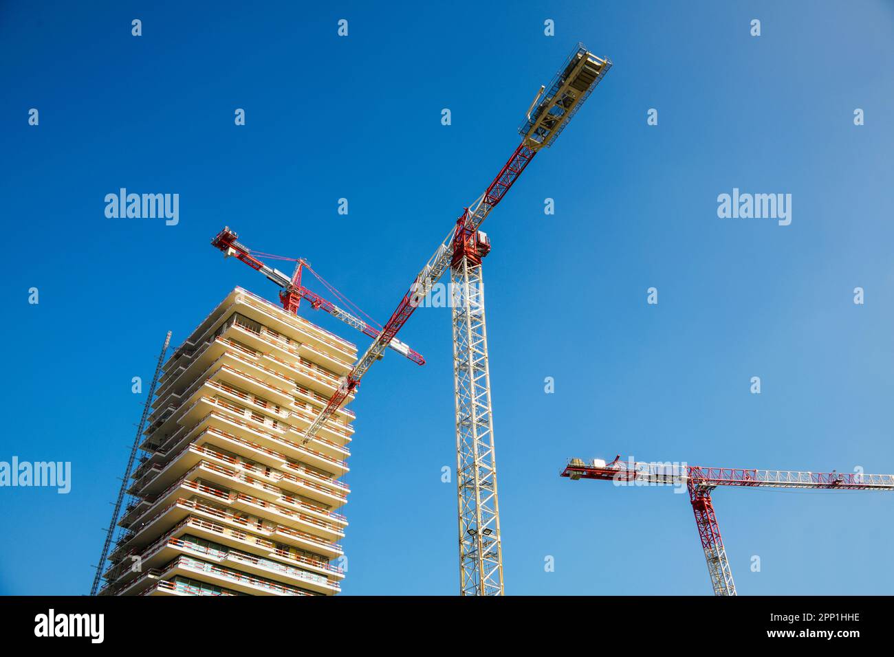 Construction cranes at a multi-story house building site, blue sky Stock Photo