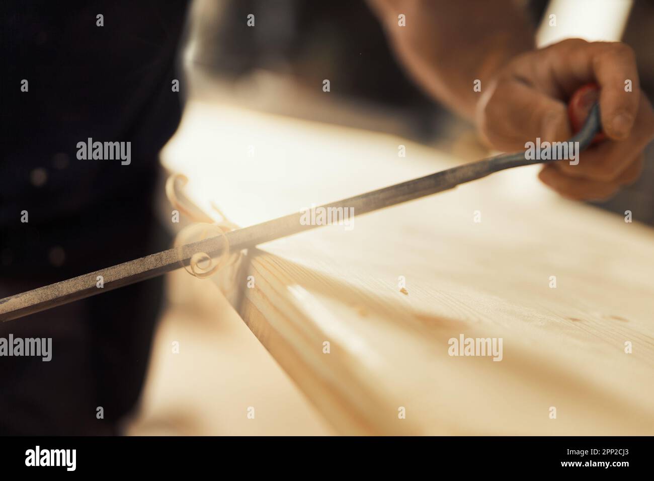 The carpenter uses a manual cutting tool to chamfer and carve the edges