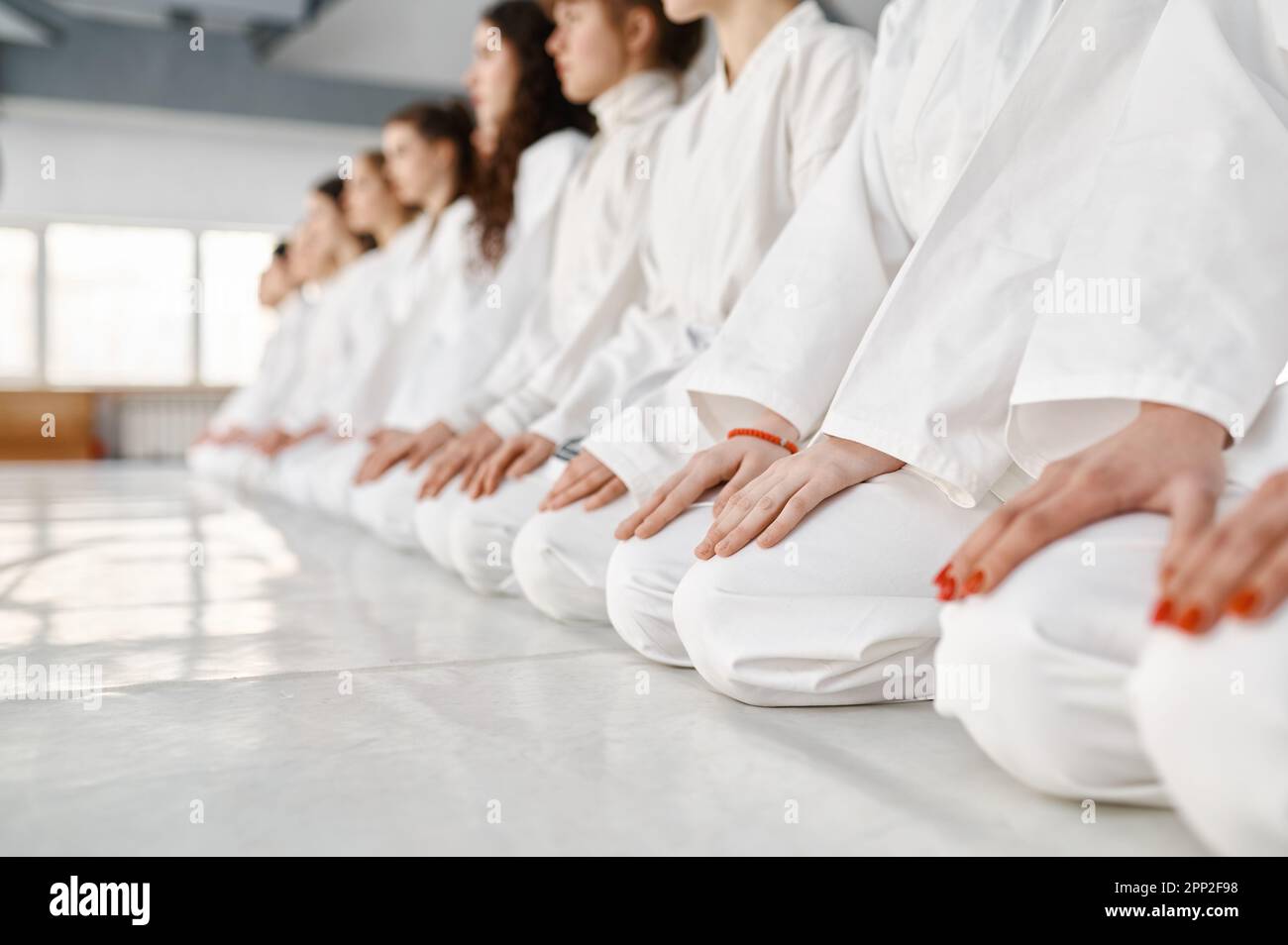 Young woman team in white martial arts uniform sitting on floor in gym