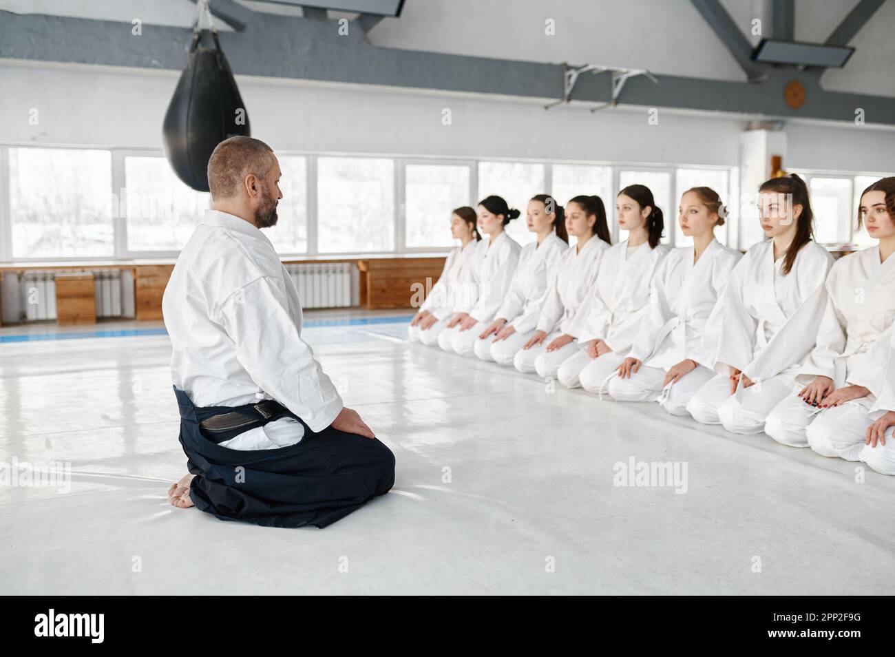 Aikido master sitting on floor front of row of young female students Stock Photo
