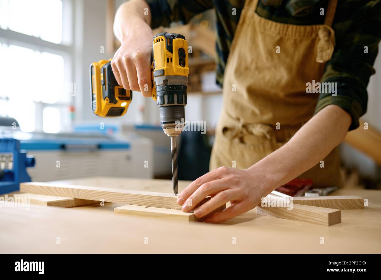 Carpenter working with drill leaning over table at carpentry workshop Stock Photo