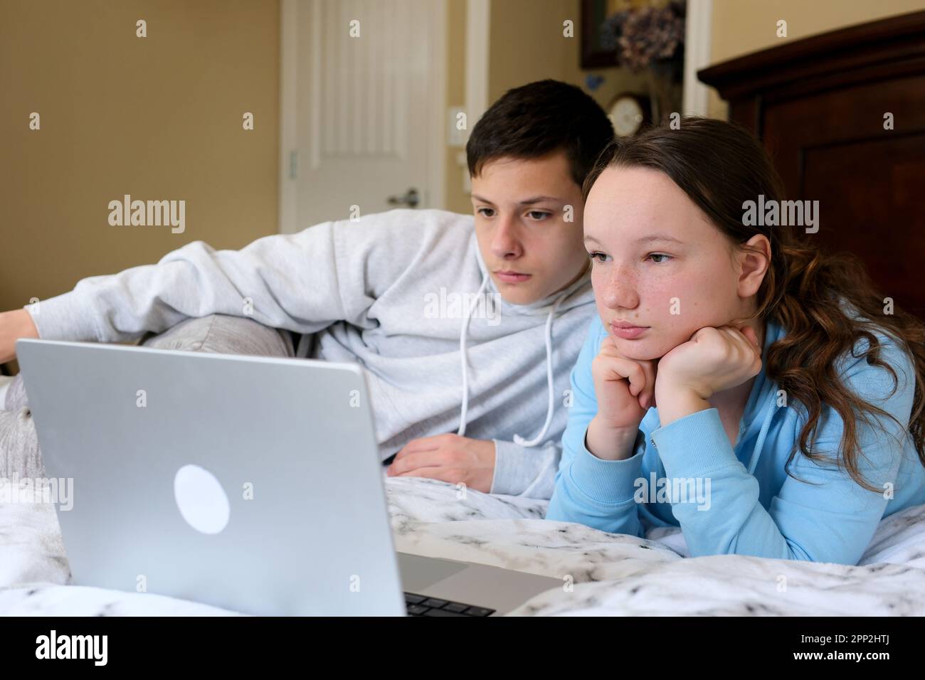 Overjoyed Kids sister brother laughing spend weekend free time together at home on couch bed eating popcorn. teen children watching video cartoon use remote control on laptop have fun Stock Photo