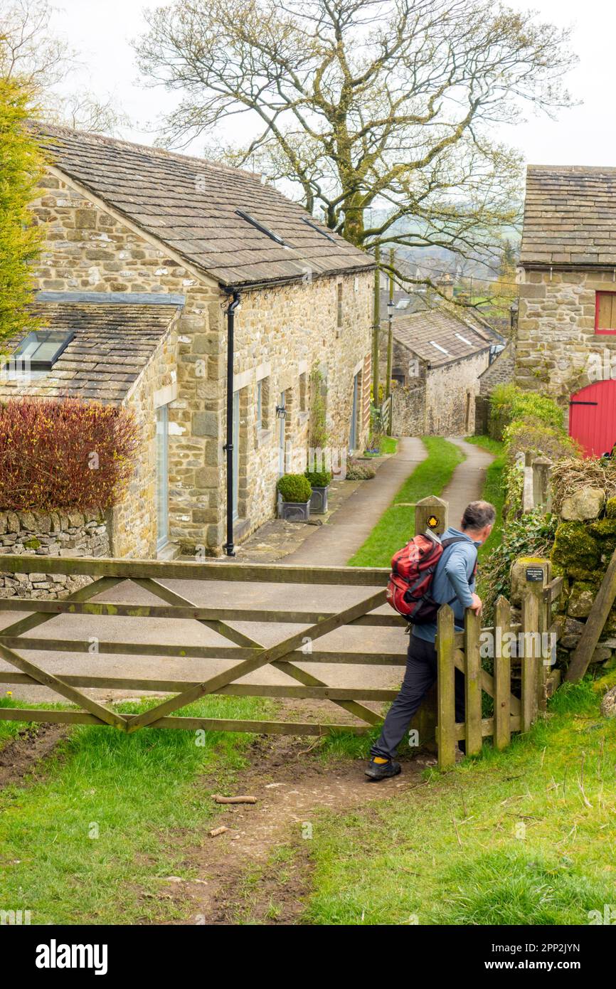 Man backpacking walking through a gate into the plague village of Eyam in the English Peak District countryside Derbyshire Stock Photo