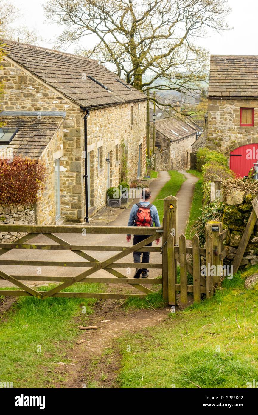 Man backpacking walking through a gate into the plague village of Eyam in the English Peak District countryside Derbyshire Stock Photo
