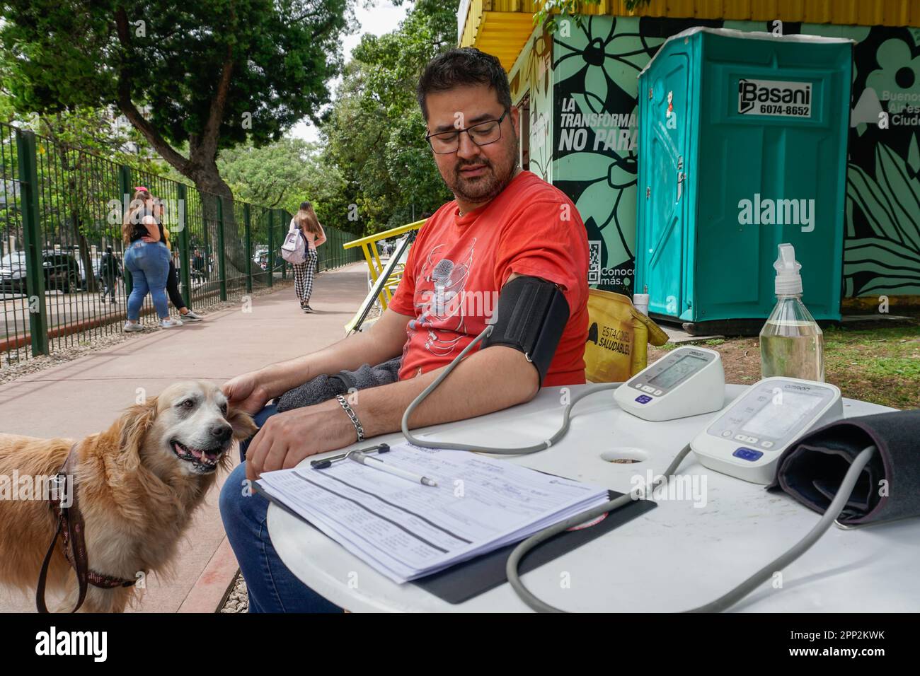 Américo Alvarado waits for a blood pressure result while petting his dog at a health station in Buenos Aires, Argentina on Oct. 19, 2022. Throughout the city, the stations offer free nutritional counseling, nursing services and recreational activities to promote health. (Lucila Pellettieri/Global Press Journal) Stock Photo