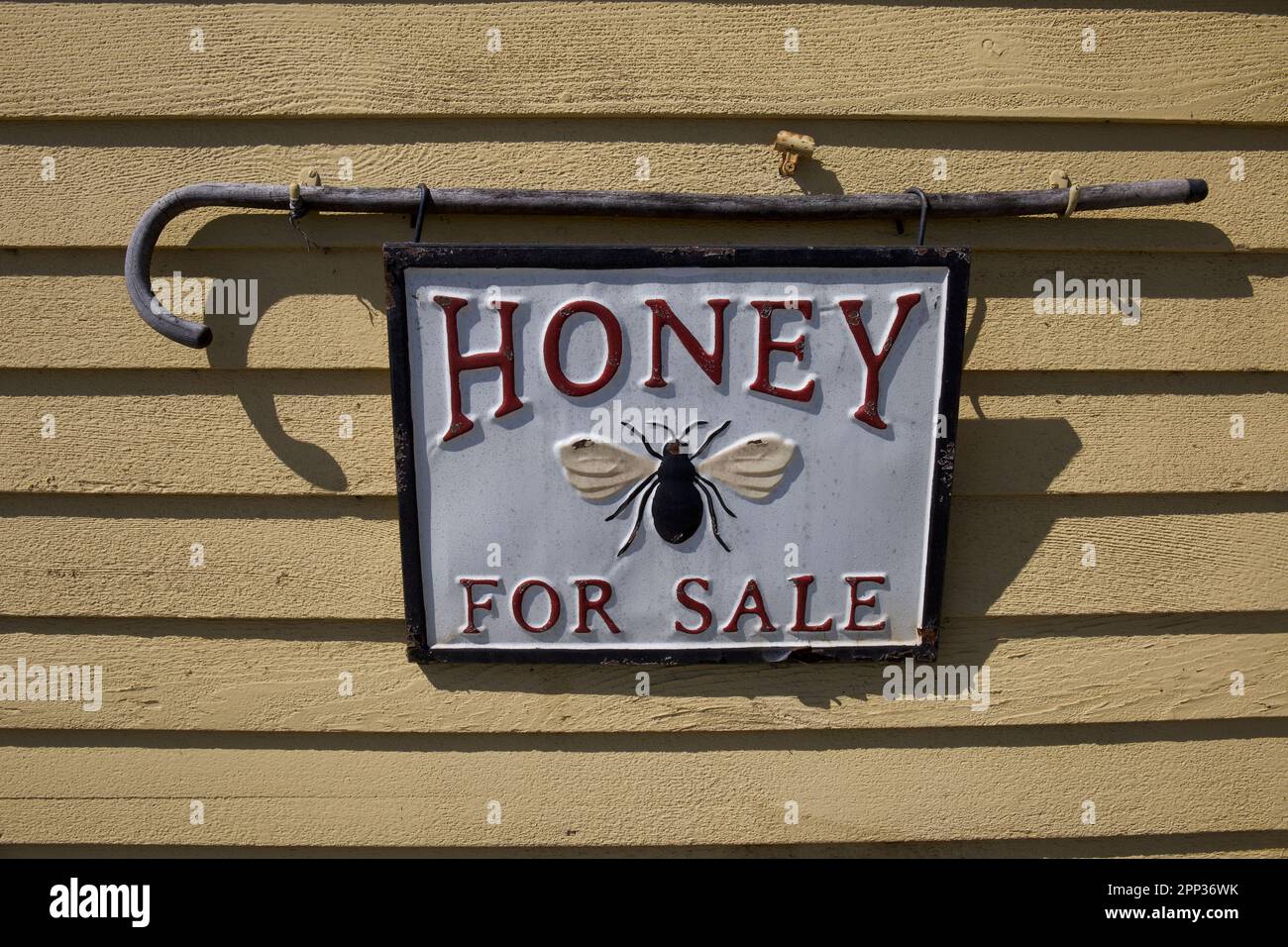 Haddam, Connecticut, USA:  building with metal sign that says HONEY FOR SALE. Bee on white sign that is held up by old walking cane. Stock Photo