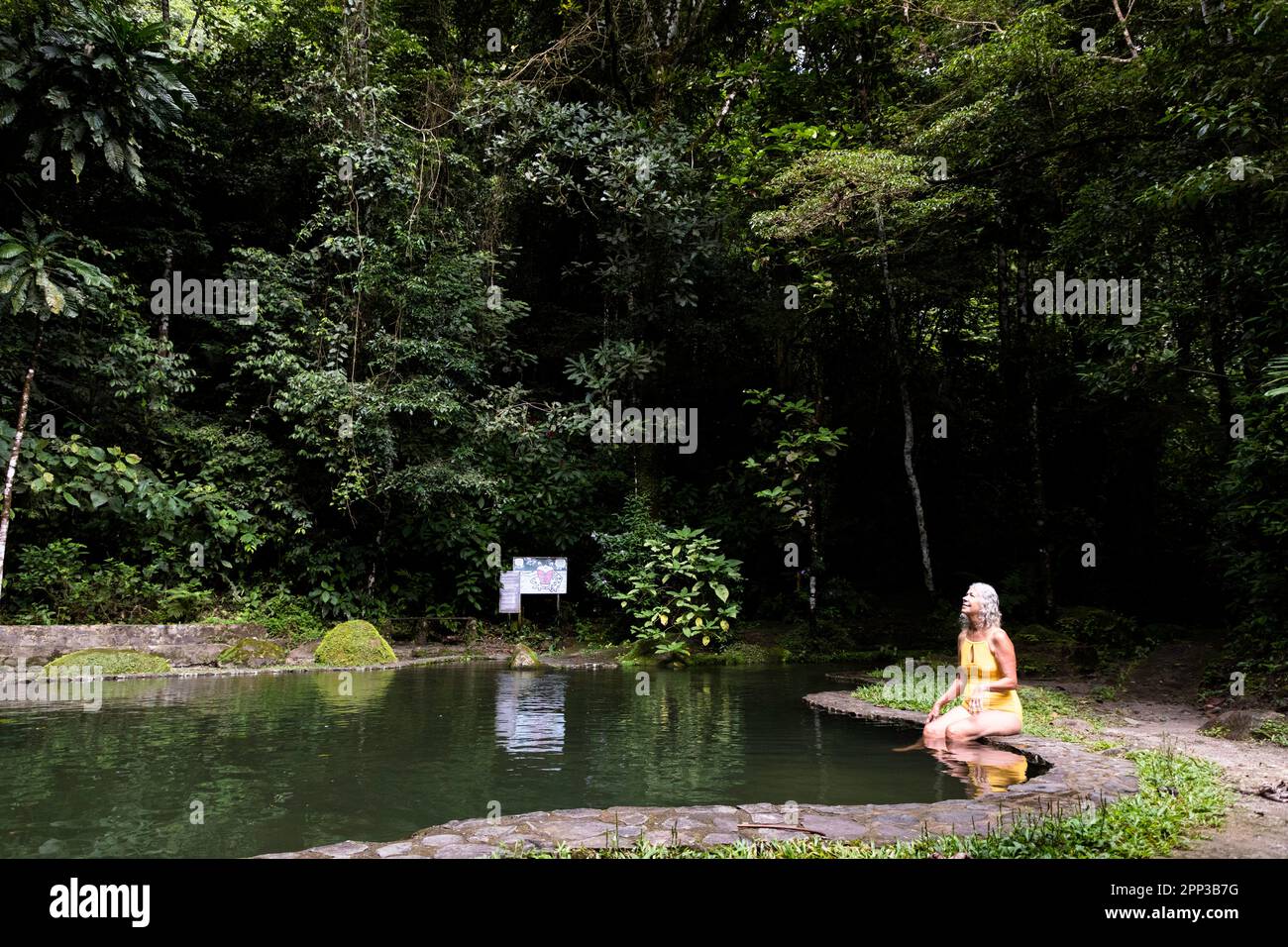 An active senior woman admires the jungle before a refreshing swim in the rain in a rock pool fed by Chorro Macho near El Valle Anton in Panama Stock Photo