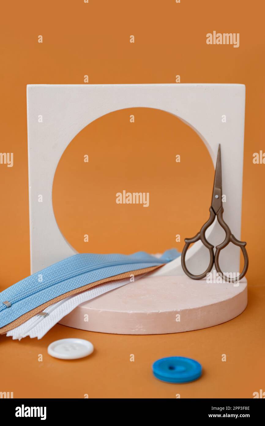 Podiums with scissors, zips and buttons on orange background Stock