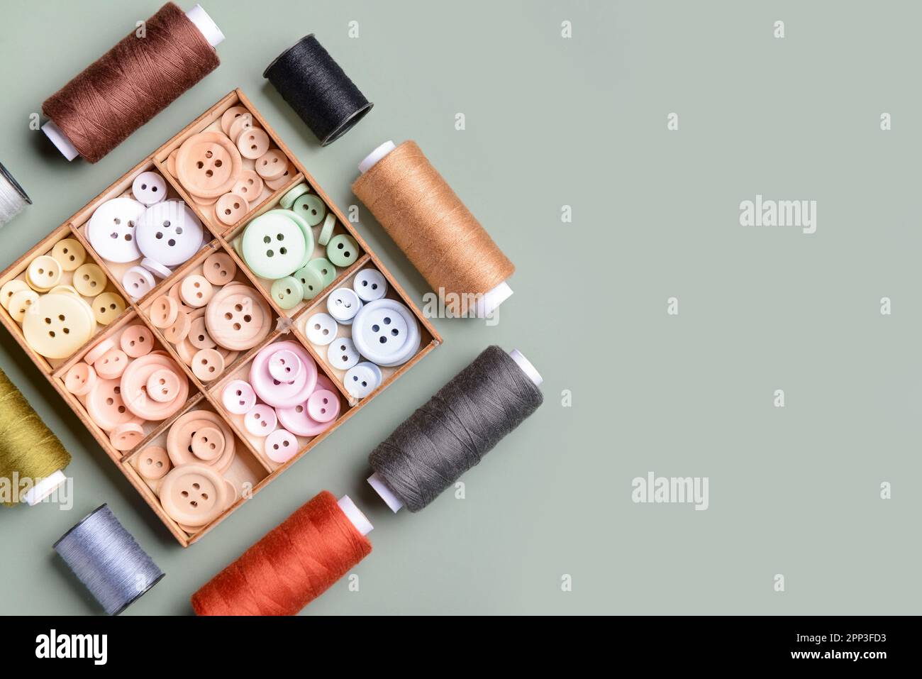 Composition with box of different buttons and thread spools on grey background Stock Photo