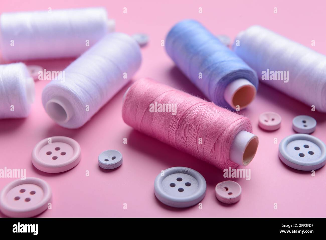 Different thread spools and buttons on pink background, closeup Stock Photo