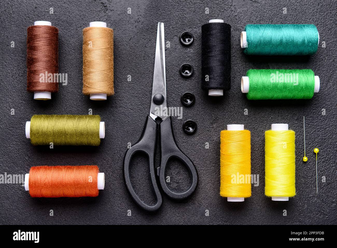 Composition with different thread spools and sewing supplies on dark background Stock Photo