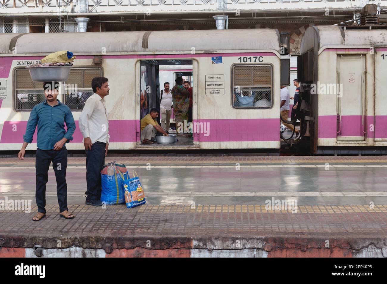 Two men waiting for a suburban train at Chhatrapati Shivaji Maharaj Terminus, Mumbai, India, one balancing a bowl with fish on his head Stock Photo