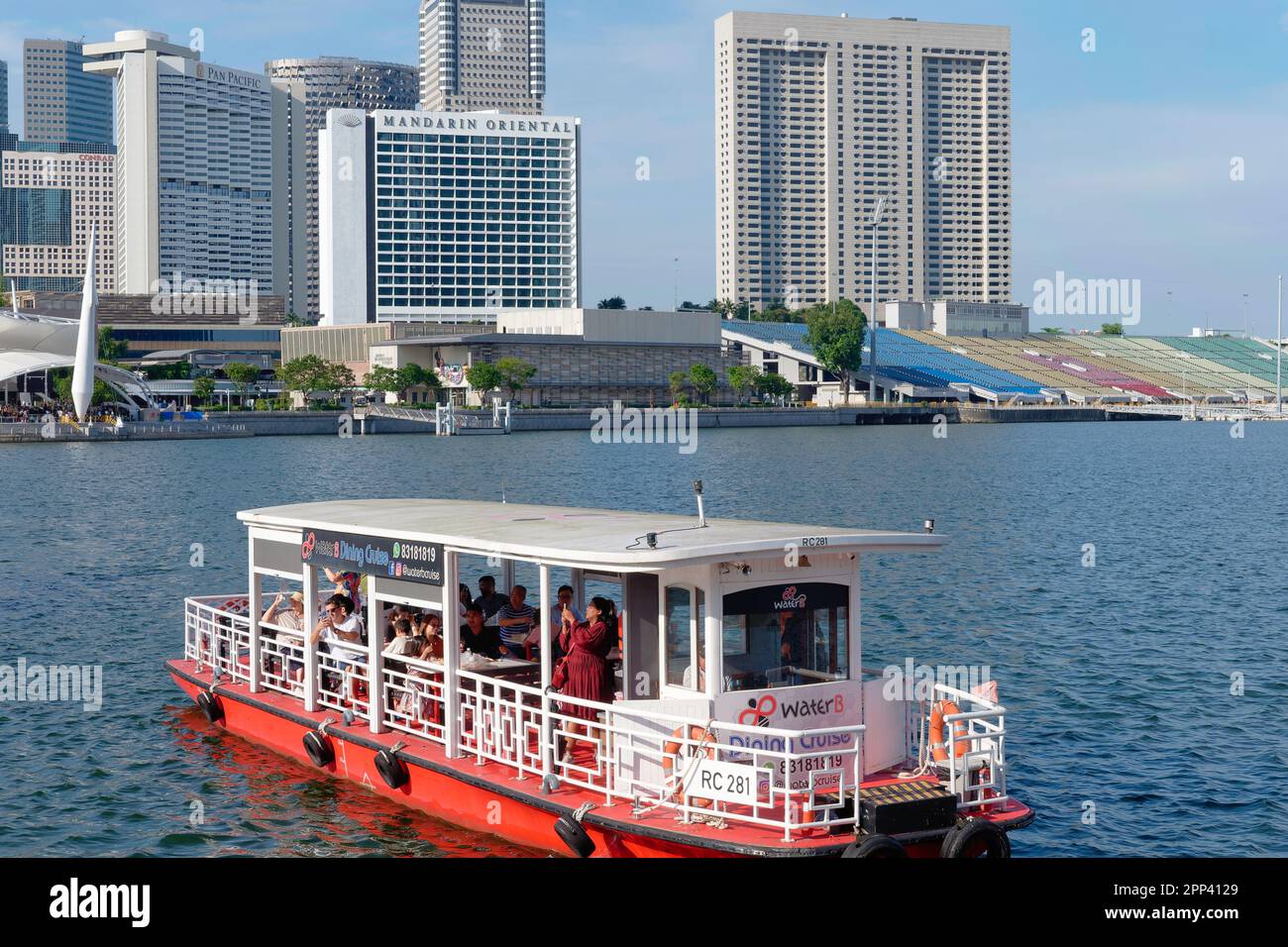 An excursion boat with tourists is cruising through Marina Bay, Singapore, with the various luxury hotels and other high rises in the background Stock Photo