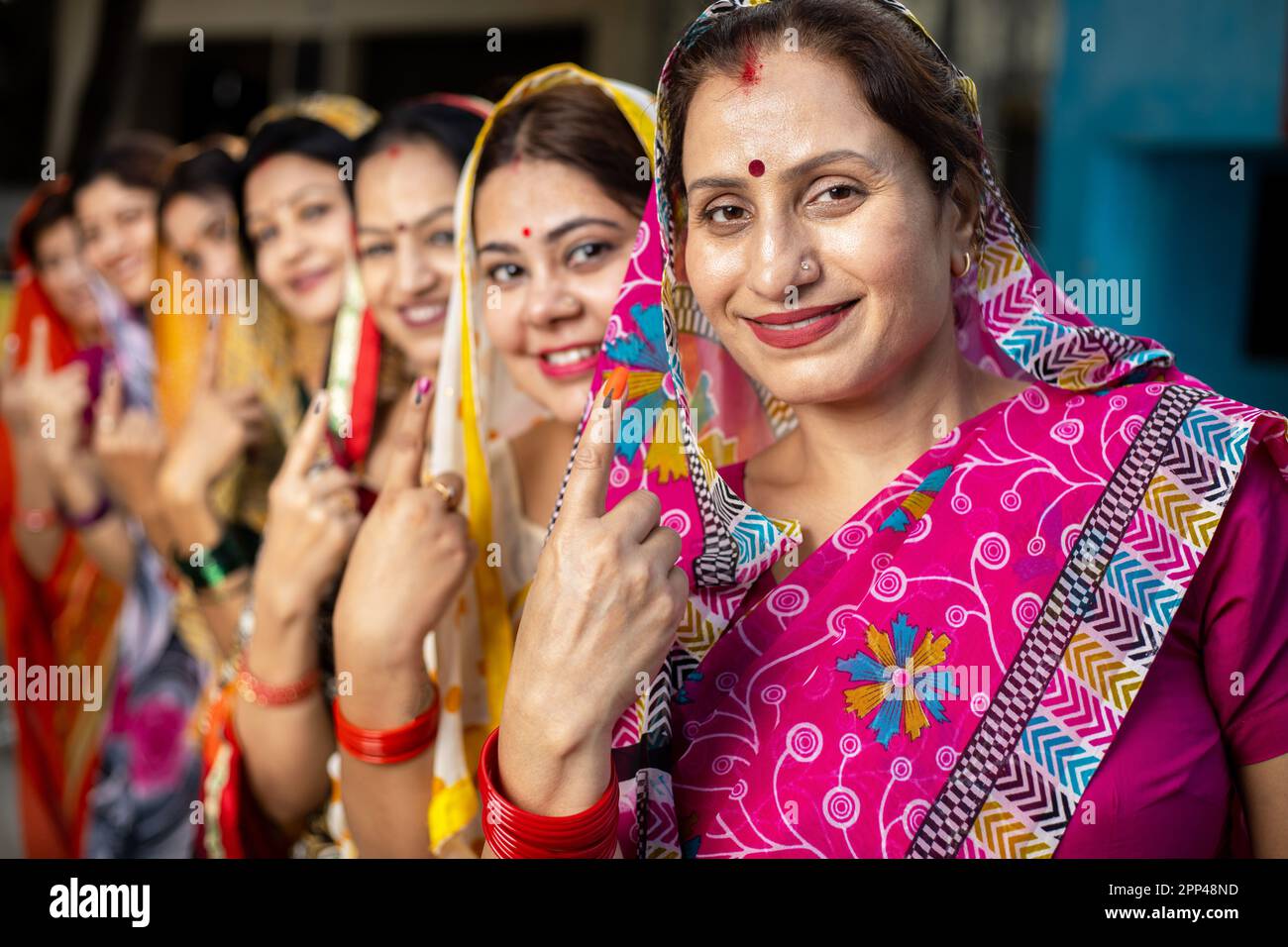 Group of happy traditional indian women standing in queue showing their finger marked with black ink after casting vote. Election in india. Stock Photo