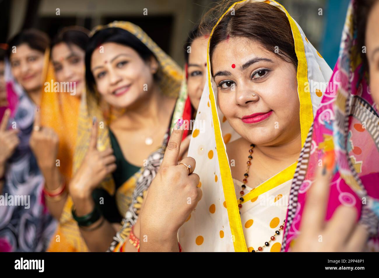 Group of happy traditional indian women standing in queue showing their finger marked with black ink after casting vote. Election in india. Stock Photo