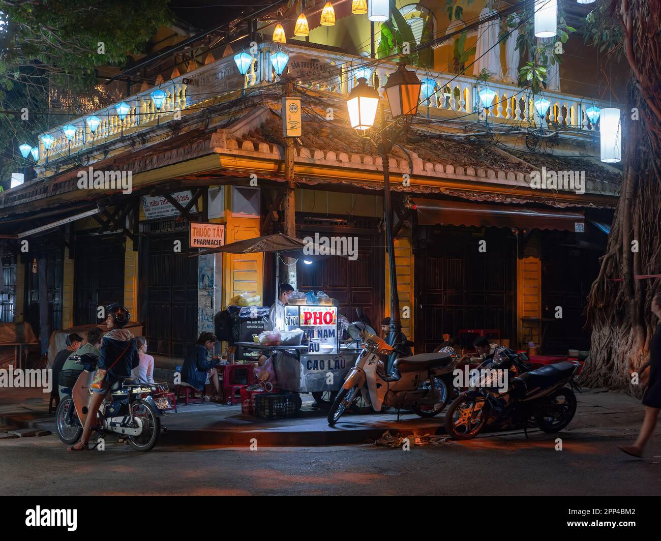 Street corner with restaurant and street food kitchen selling noodles in Hoi An, Quang Nam province, Vietnam at night. The old city of Hoi An is a Wor Stock Photo