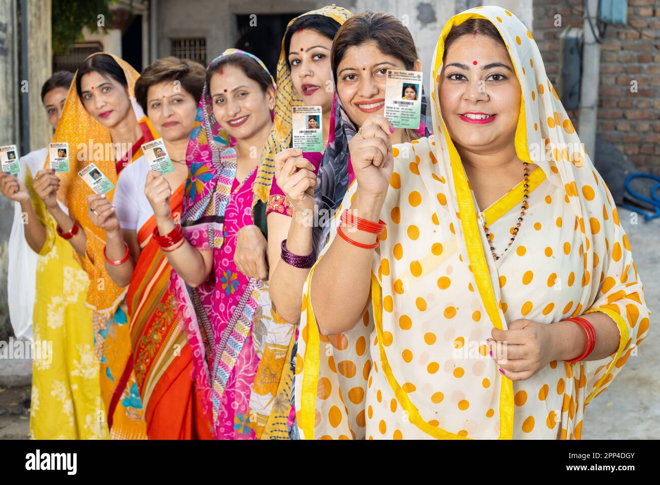 Group of happy traditional indian women standing in queue showing voter card id to cast vote at polling station. Election in india. Stock Photo
