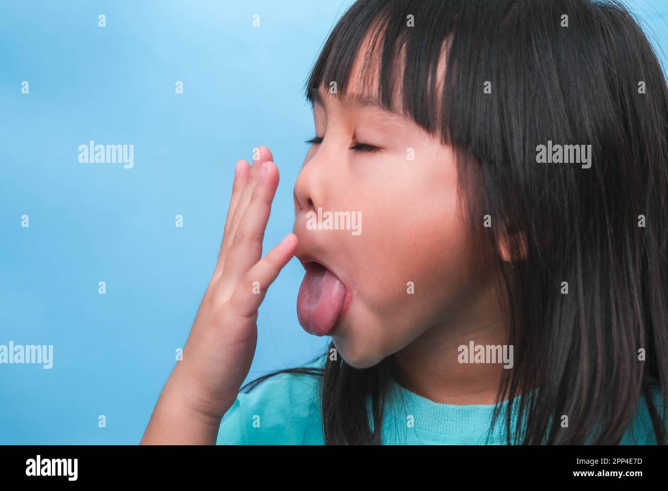 Little asian girl covering her mouth to smell the bad breath. Child girl checking breath with her hands. Oral health problems or dental care concept. Stock Photo