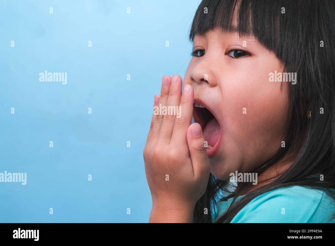 Little asian girl covering her mouth to smell the bad breath. Child girl checking breath with her hands. Oral health problems or dental care concept. Stock Photo
