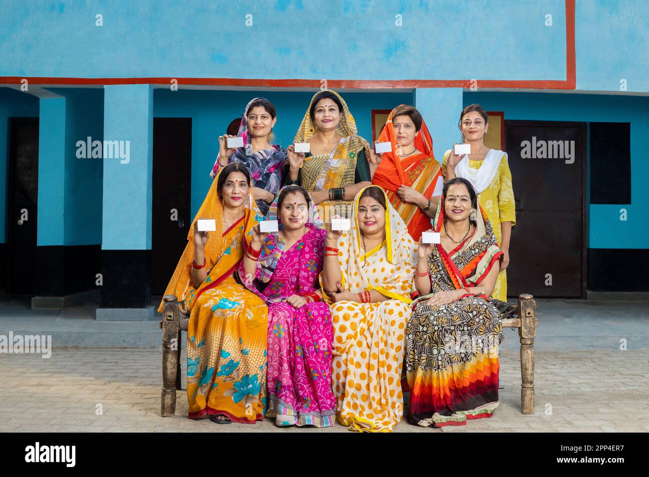 Group of happy traditional indian women wearing sari sitting together showing blank id or business card. Mockup. Stock Photo
